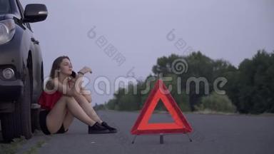 心烦意乱的女孩坐在她失事的车旁边年轻的女人坐在失事的车旁边悲伤的女人正在打电话